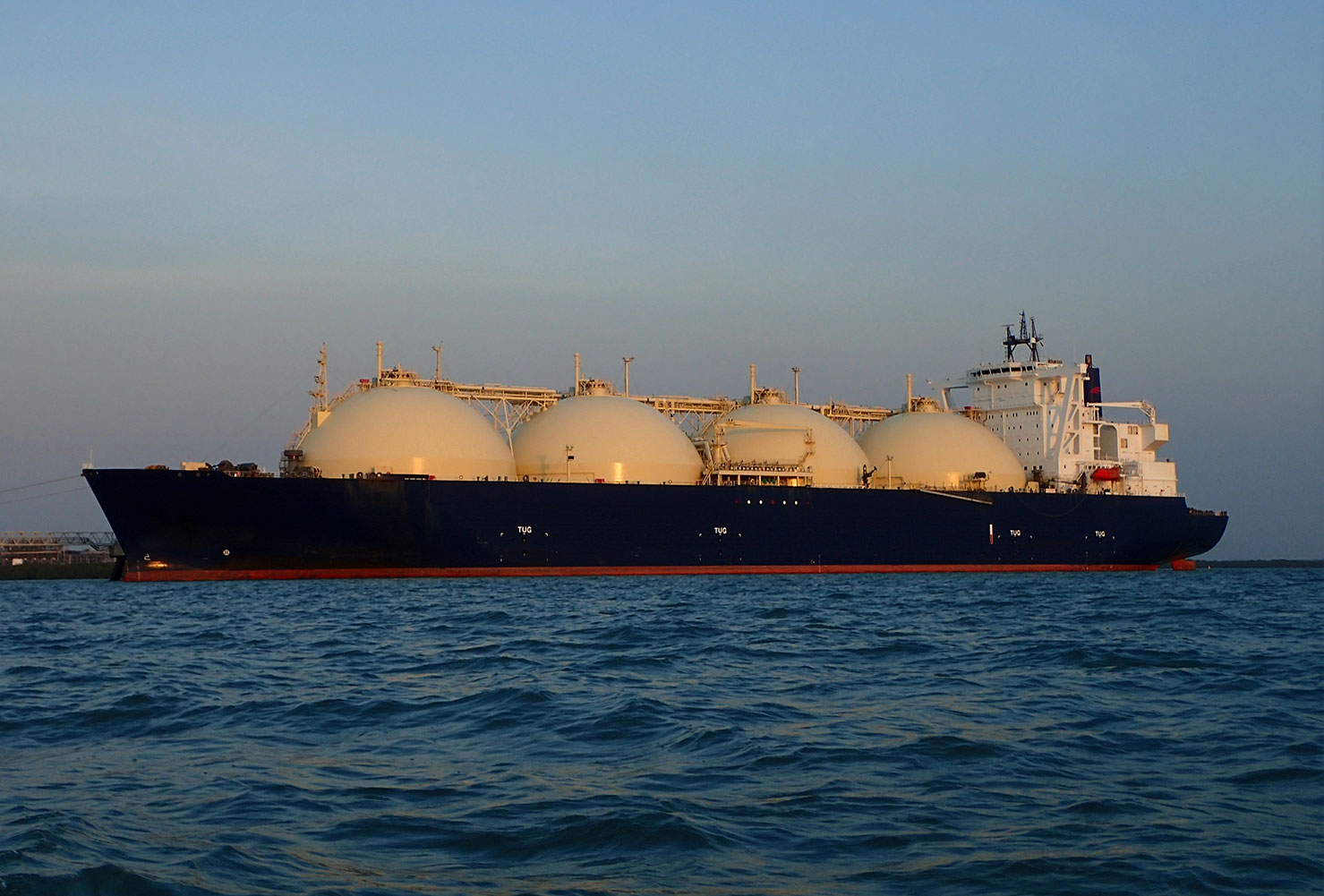 Gas-Reservation-Policy-Blog A large liquefied natural gas (LNG) tanker ship with multiple spherical storage tanks on its deck, floating on calm ocean waters during sunset or early evening