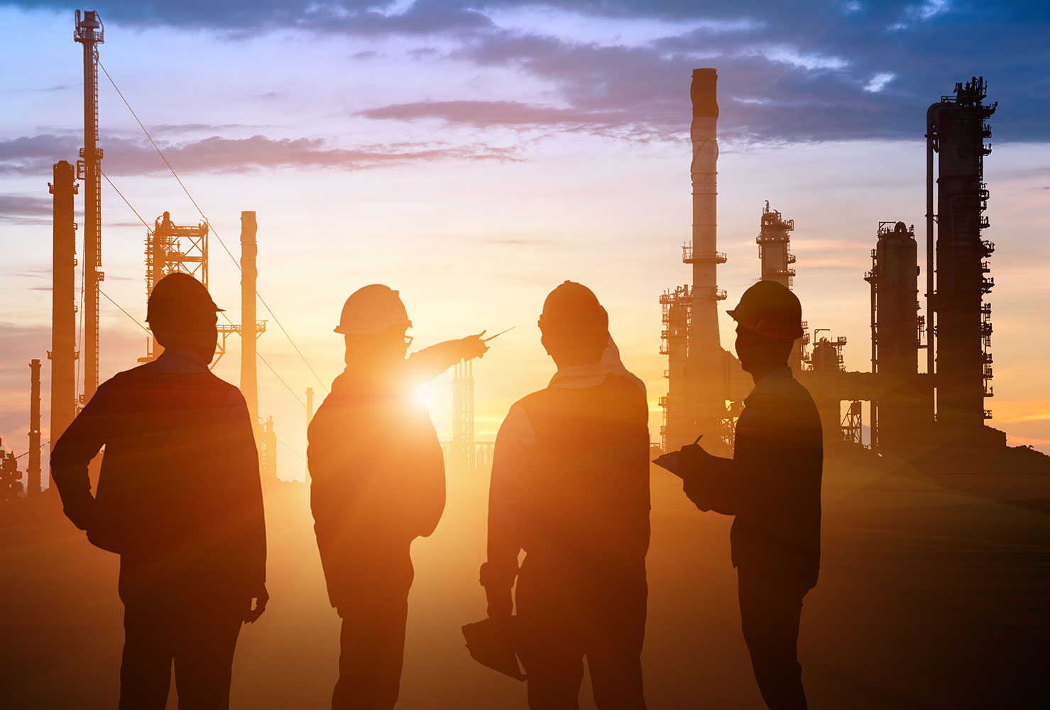 Silhouettes of four workers wearing hard hats and safety vests standing in front of an industrial oil or gas refinery during sunset, with one worker pointing toward the facility and another holding a clipboard.