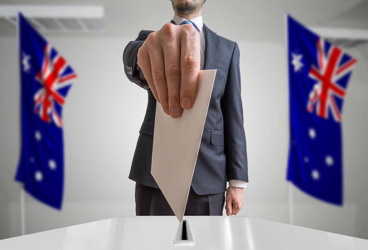 Election in Australia. Voter holds envelope in hand above ballot. Australian flags in background.