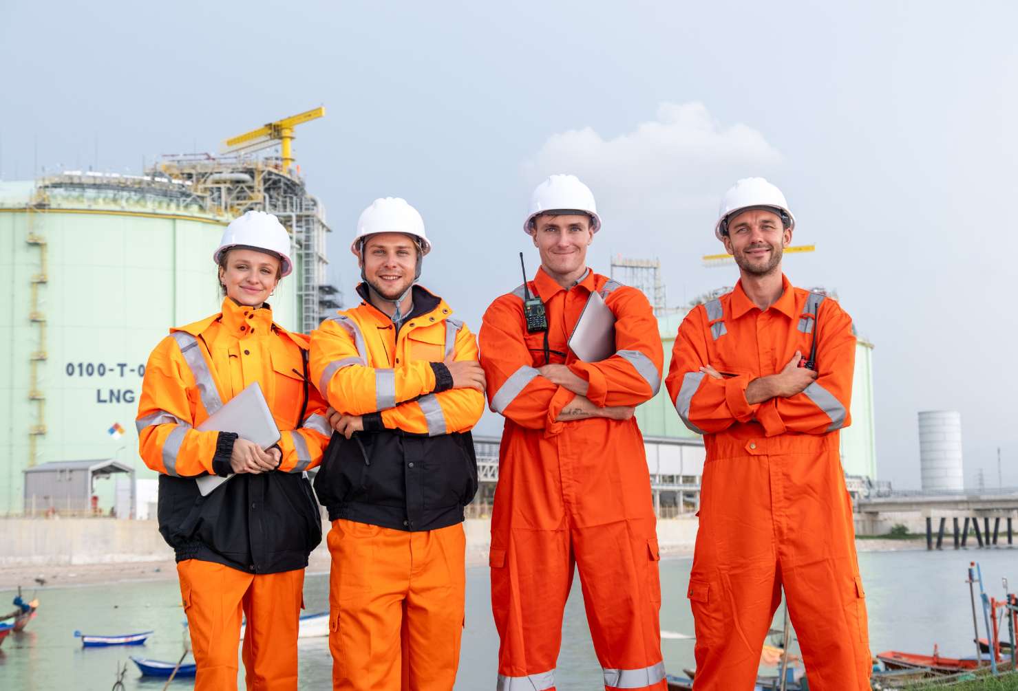 Four workers in safety gear pose by LNG storage tanks at an industrial site during the day