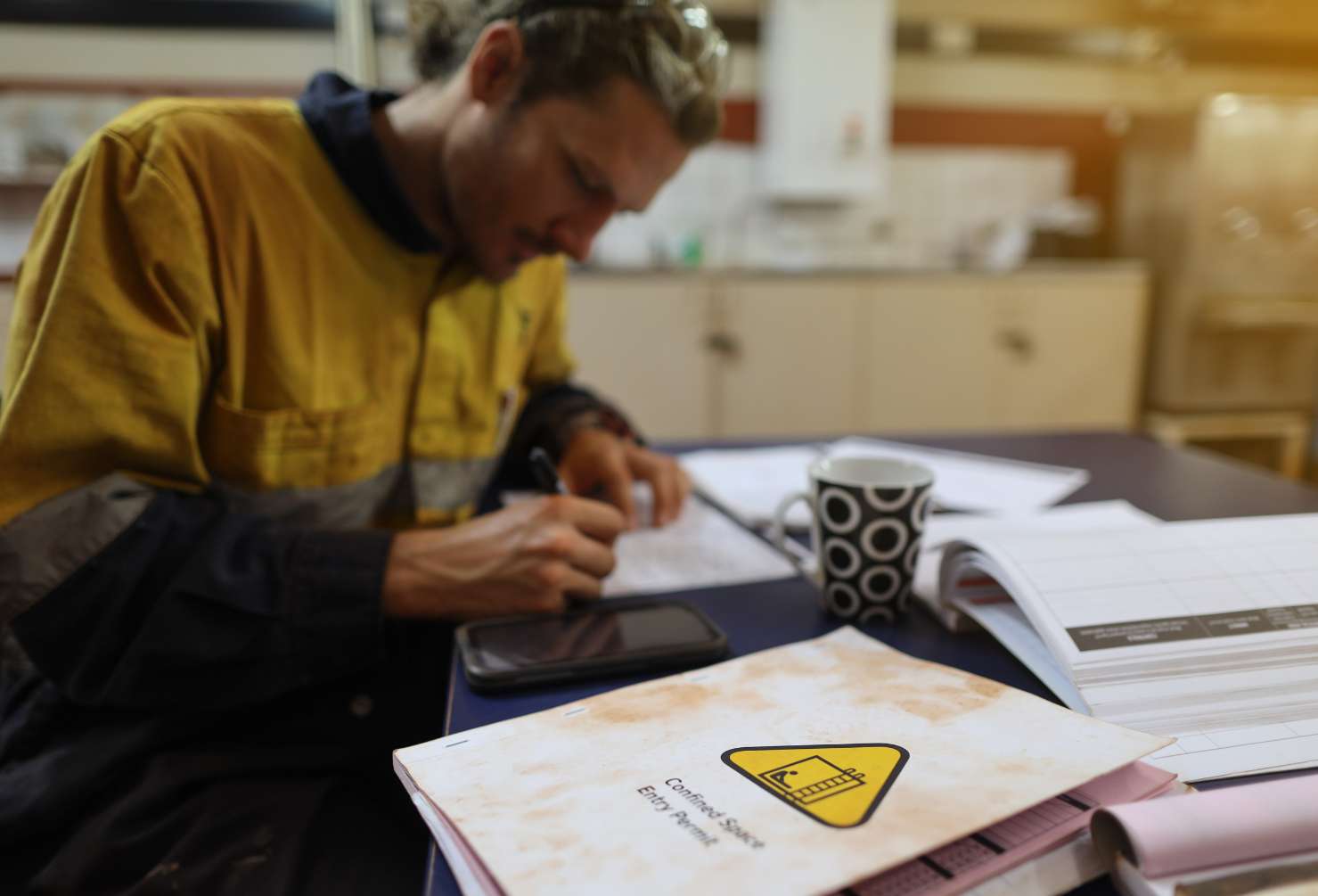 Occupational health and safety closeup picture of confined spaces permit book placing on the table with defocused worker conducting writing job hazard analysis risk assessment safety auditor