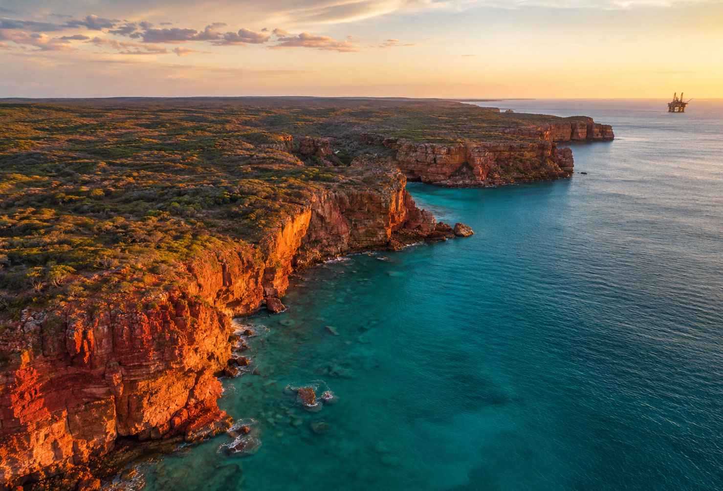 Aerial view of the Kimberley coastline Western Australia, red cliffs, turquoise water, offshore gas platform visible in the distance