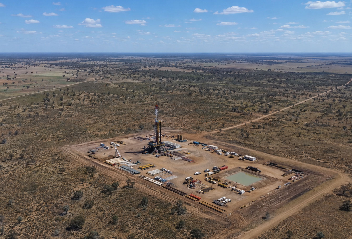 Aerial photograph of a gas exploration drilling site on the Western Downs Queensland Australia, flat rural landscape with scrub and paddocks, a drilling rig and site infrastructure visible from above, wide open sky,