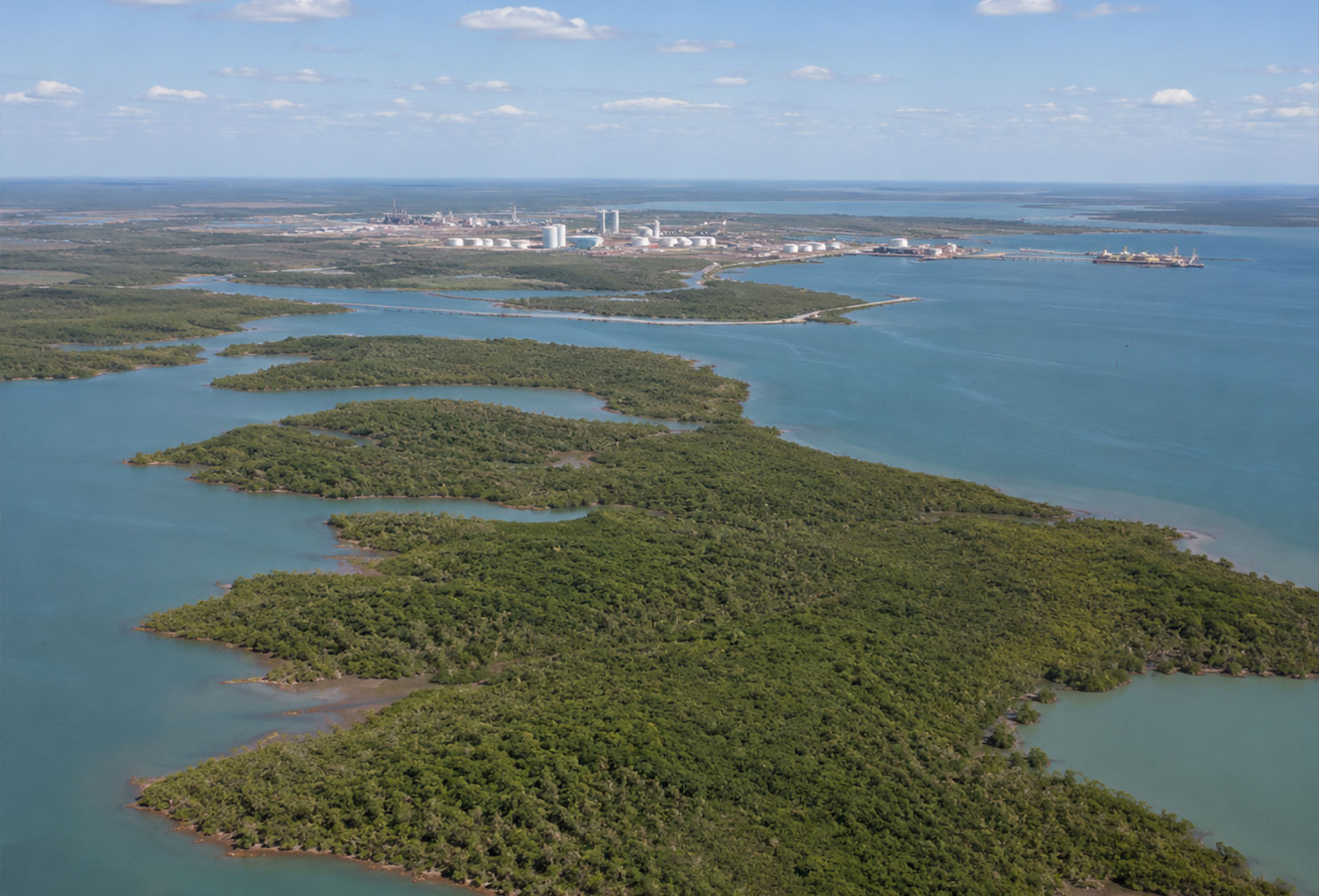 Aerial view of a large undeveloped tropical peninsula near Darwin Northern Territory, calm blue harbour water, industrial development concept visible in the distance,